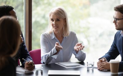 Confident focused middle-aged businesswoman head team meeting with diverse colleagues, consider paperwork together, concentrated female boss talk brainstorm discuss business project with coworkers